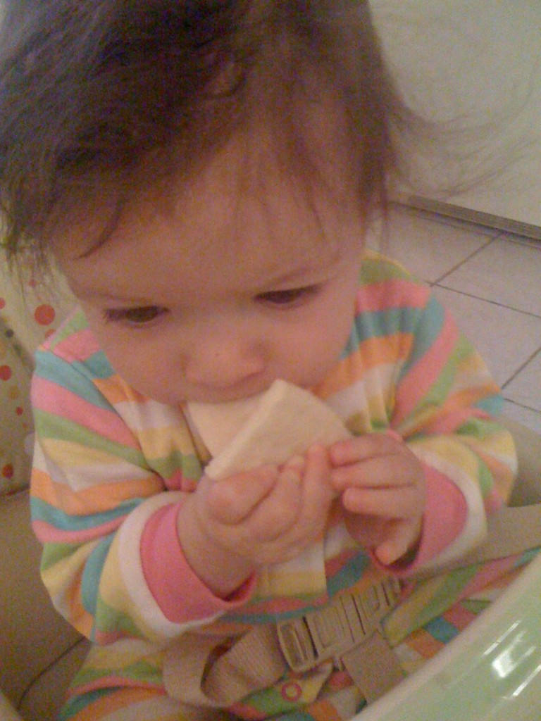 Enjoying solid food, but have not yet mastered getting it into her mouth